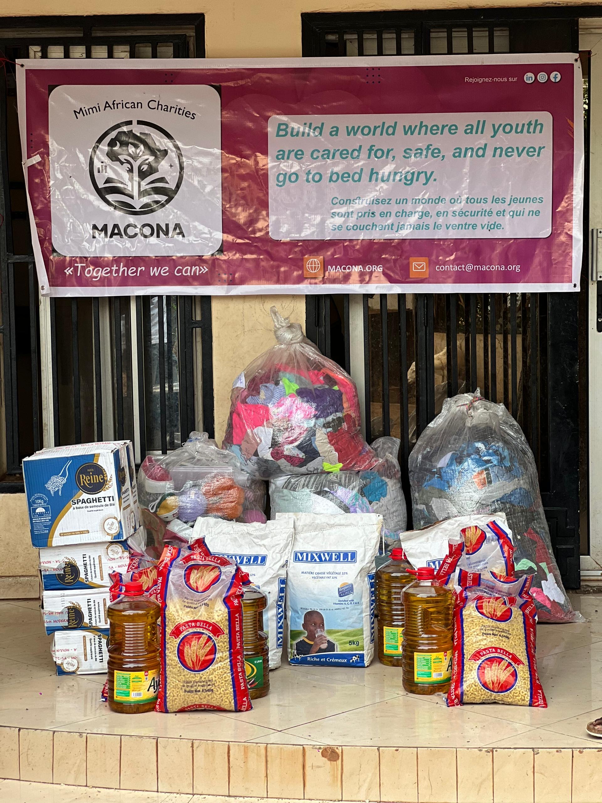 MACONA donations staged under banner — food, oil, clothing bags ready for shipment