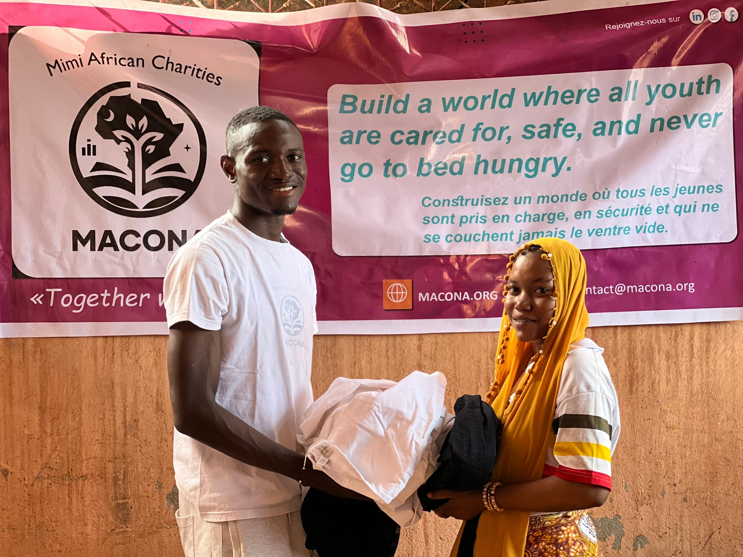 MACONA volunteer handing donated clothing to young woman in front of MACONA banner