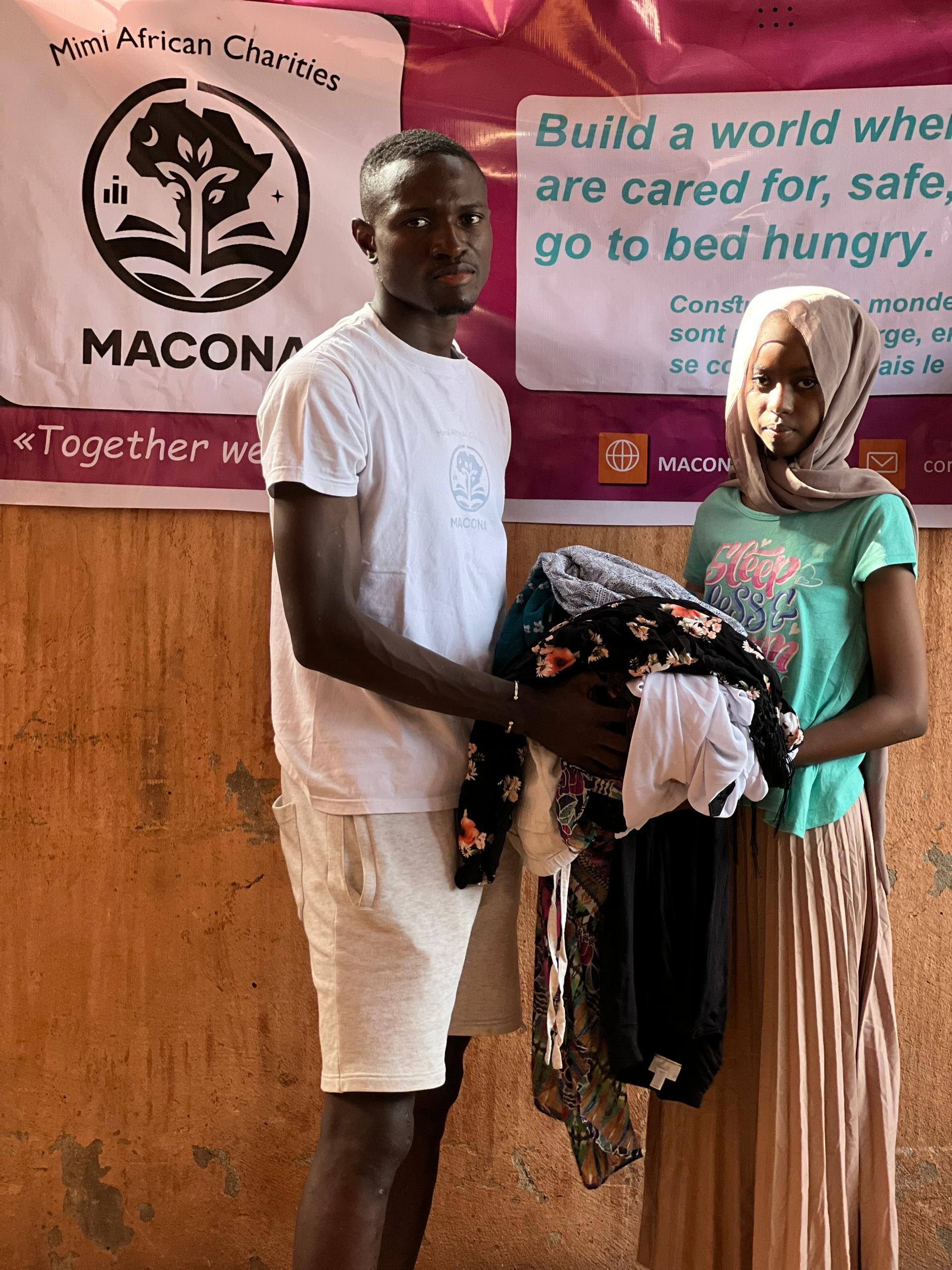 A staff member handing clothes to a young girl with her head covered