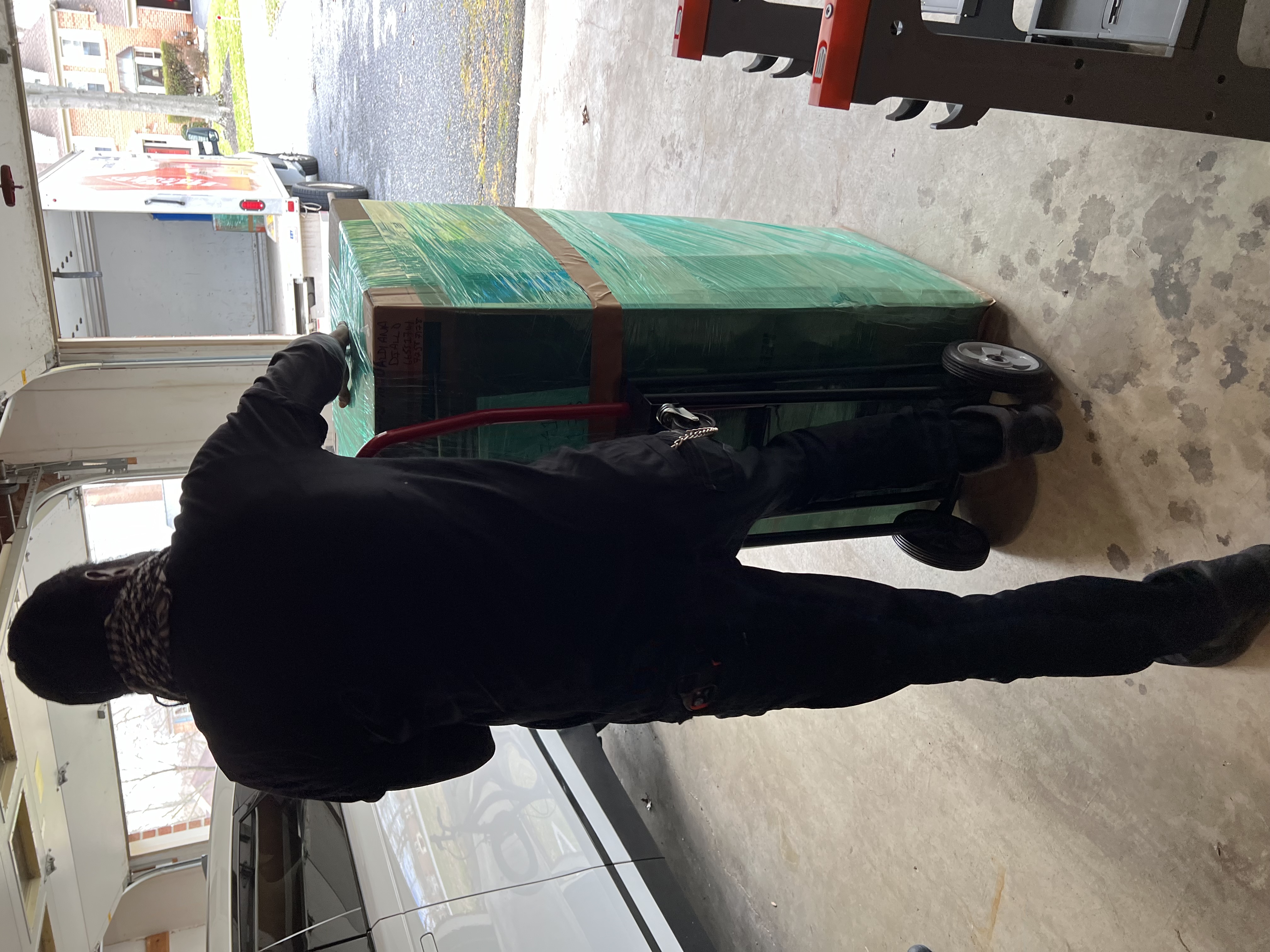 Volunteer moving a large wrapped donation box on a dolly inside a garage