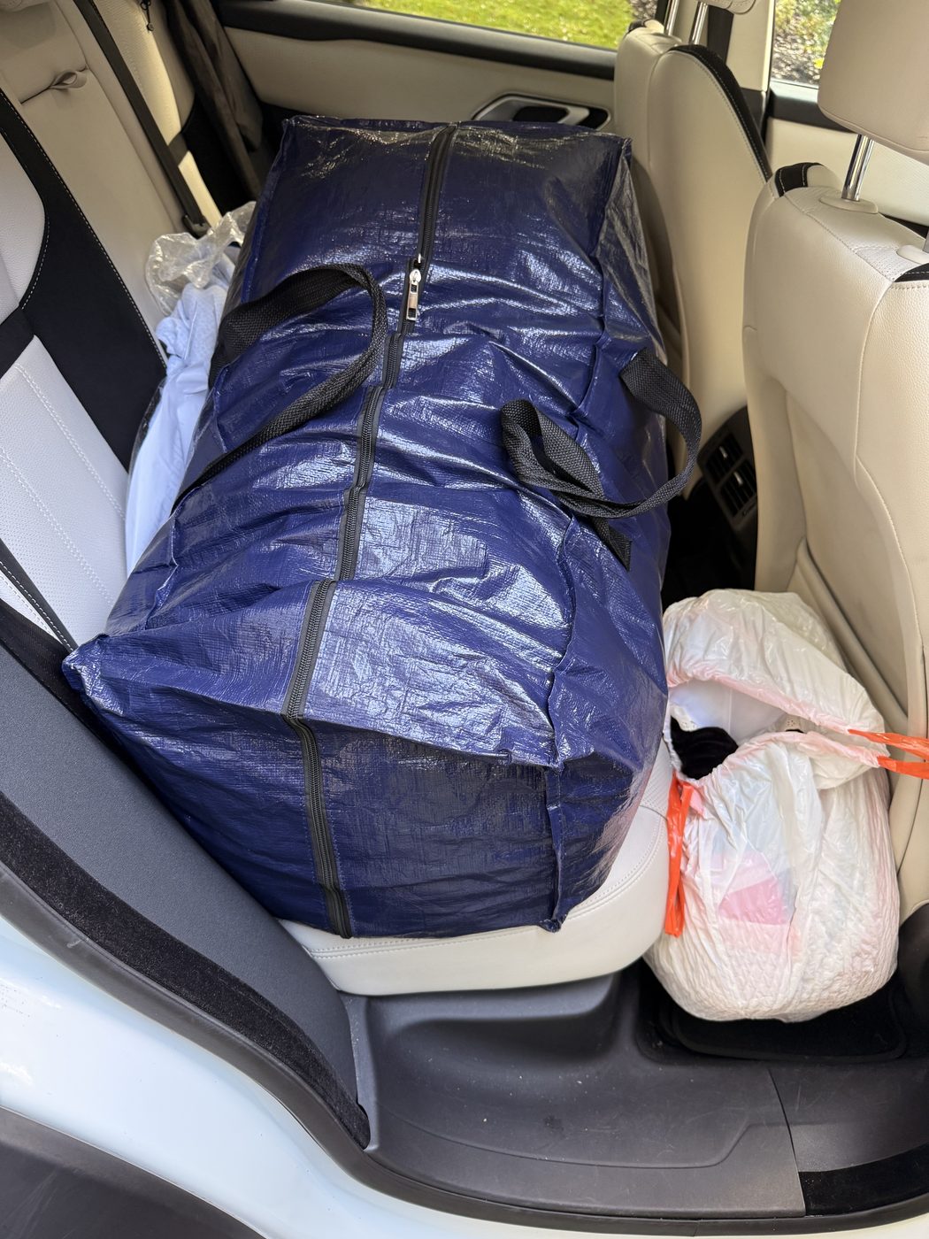 A large blue tote bag and a white bag of donations loaded onto a car seat in Maryland